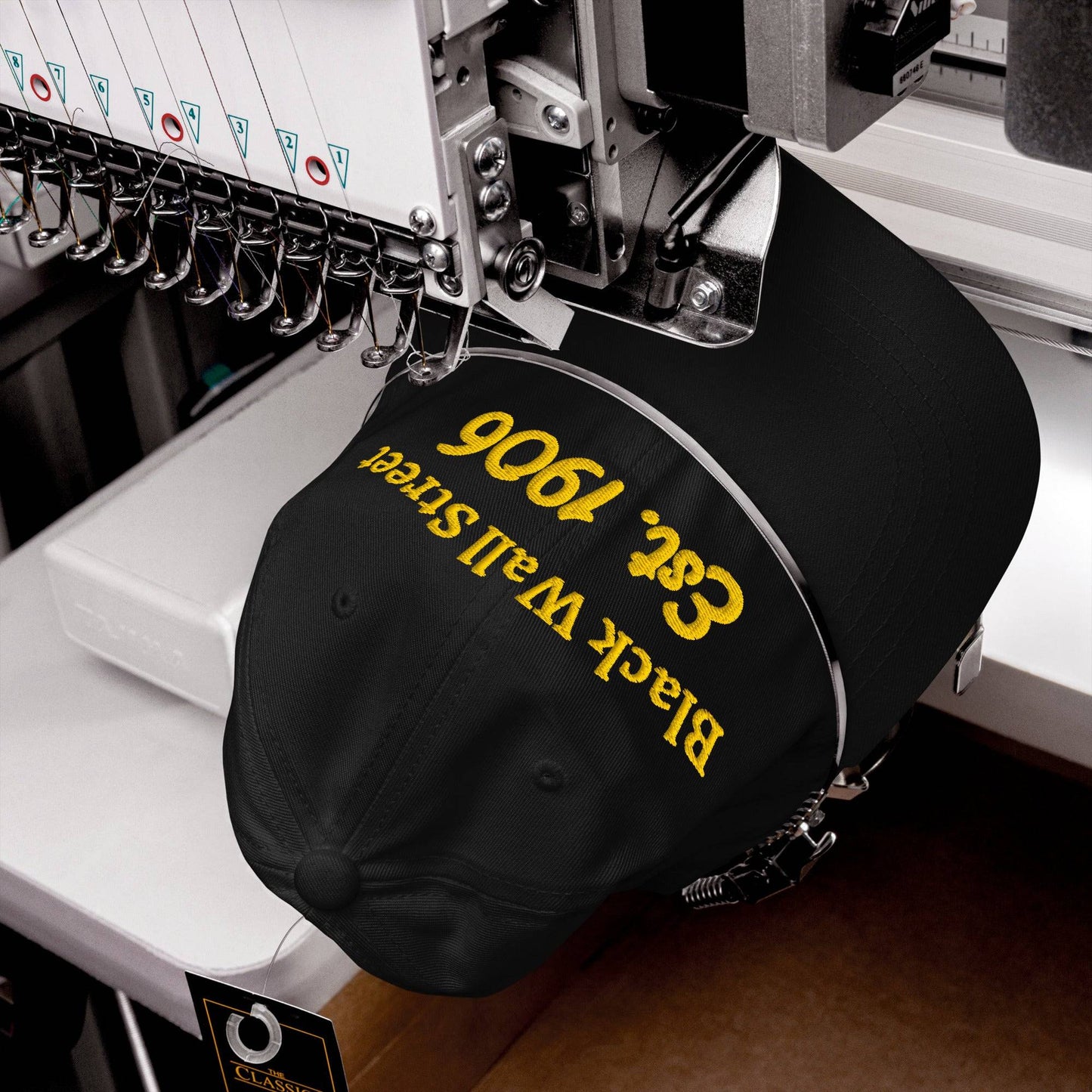 Black Wall Street Est. 1906 Baseball Cap being embroidered on a machine, showcasing craftsmanship and USA production.