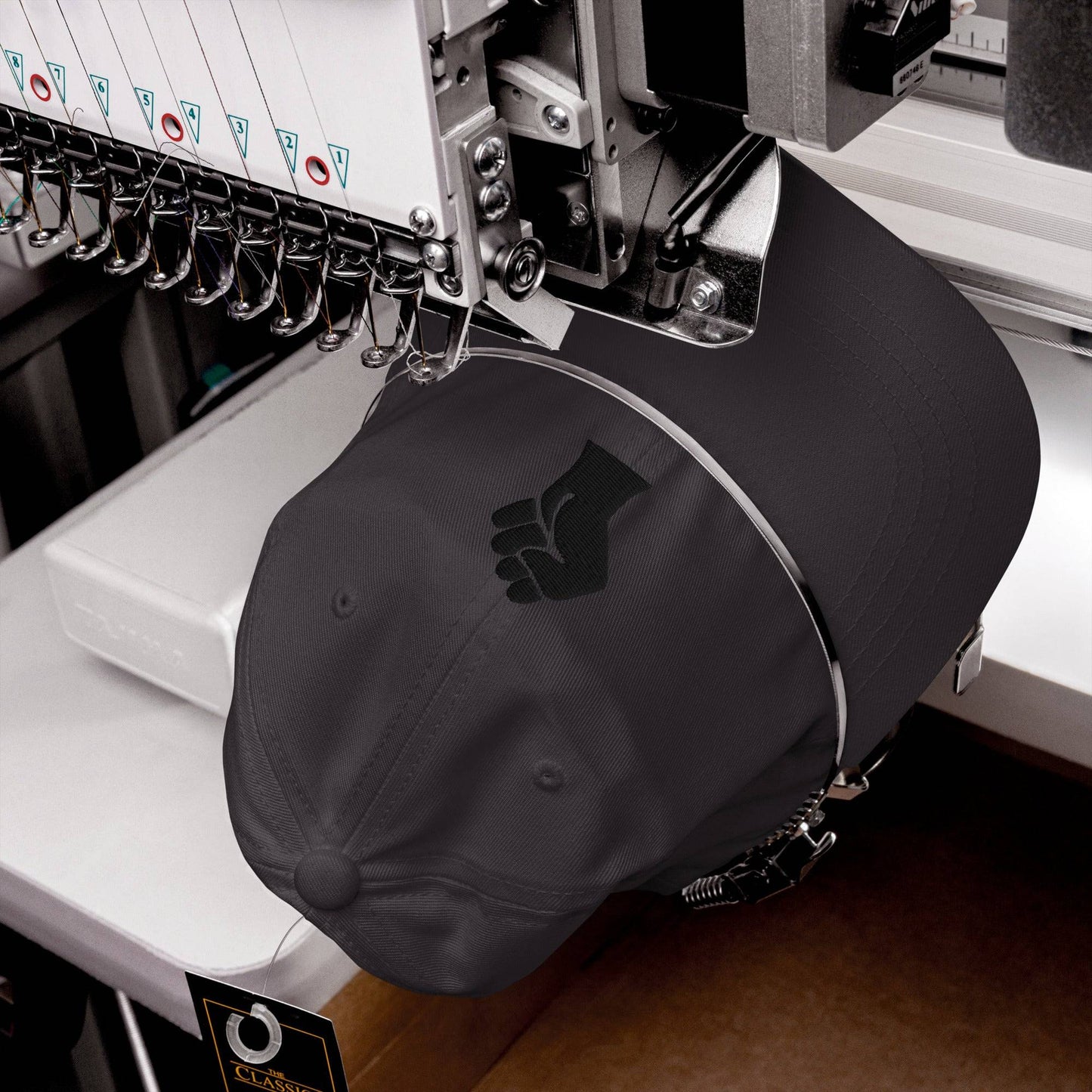 Black On Black Power Fist Embroidered Baseball Cap being stitched on embroidery machine, showcasing quality craftsmanship.