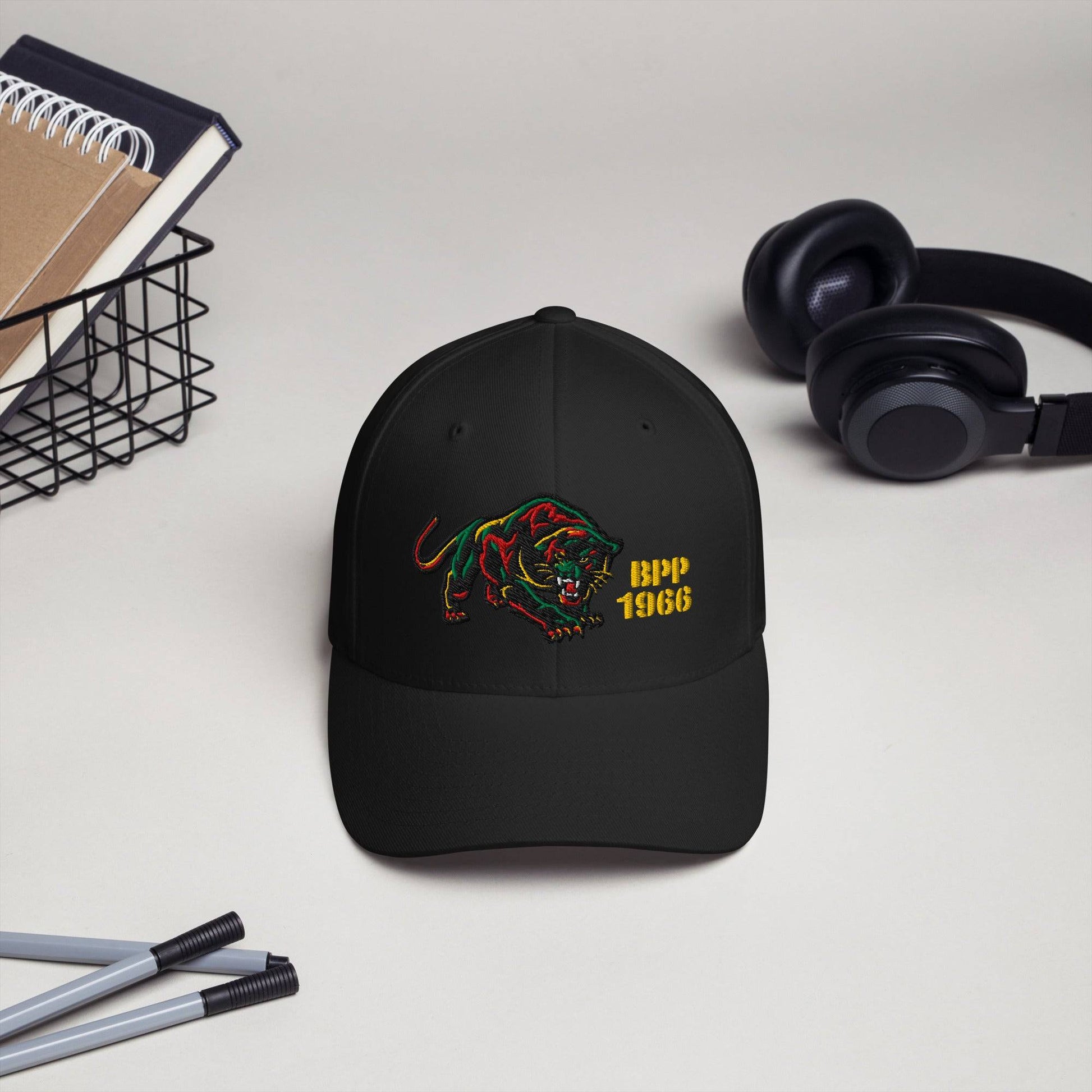 Black BPP 1966 Flexfit cap displayed on desk with headphones and stationery, showcasing embroidered Black Panther Party design.