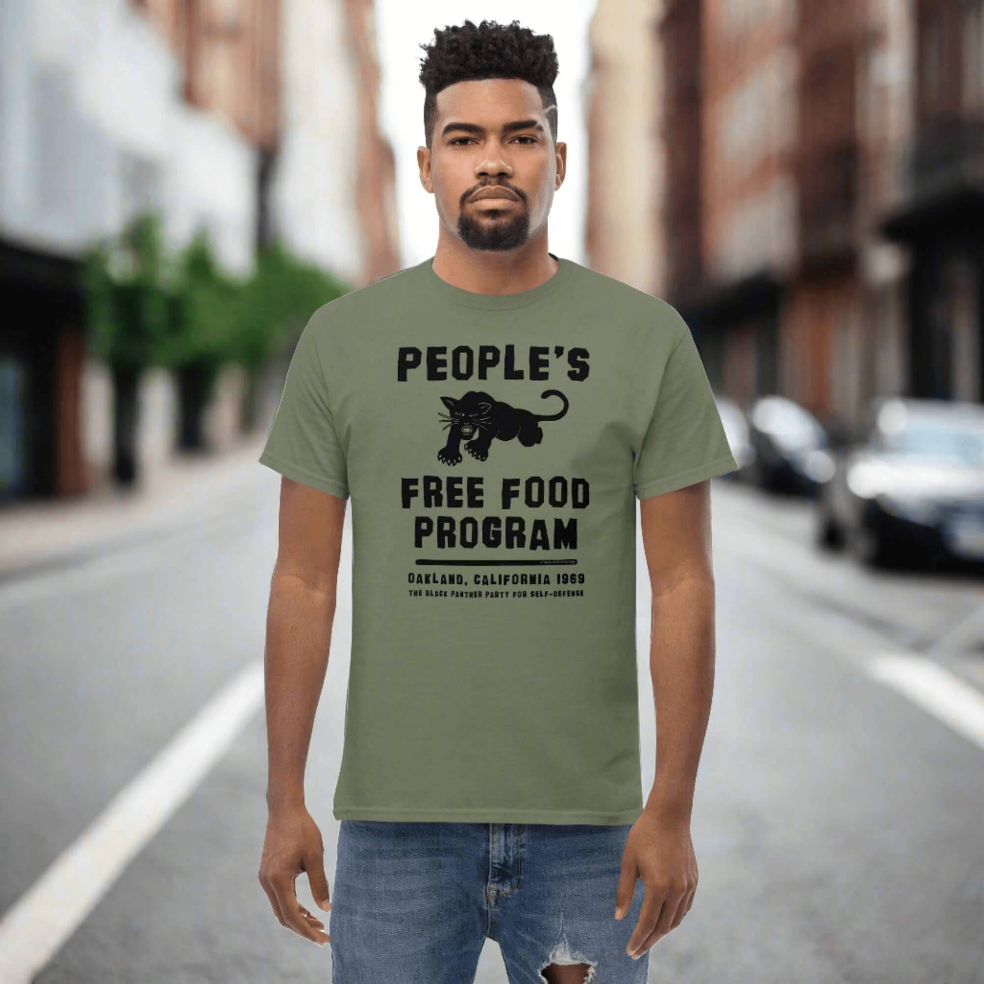 People's Free Food Program Staple T-Shirt in olive green, featuring a bold black panther graphic and text honoring the Black Panther Party's initiative. Made from 100% cotton, this unisex graphic tee celebrates Black history and activism.