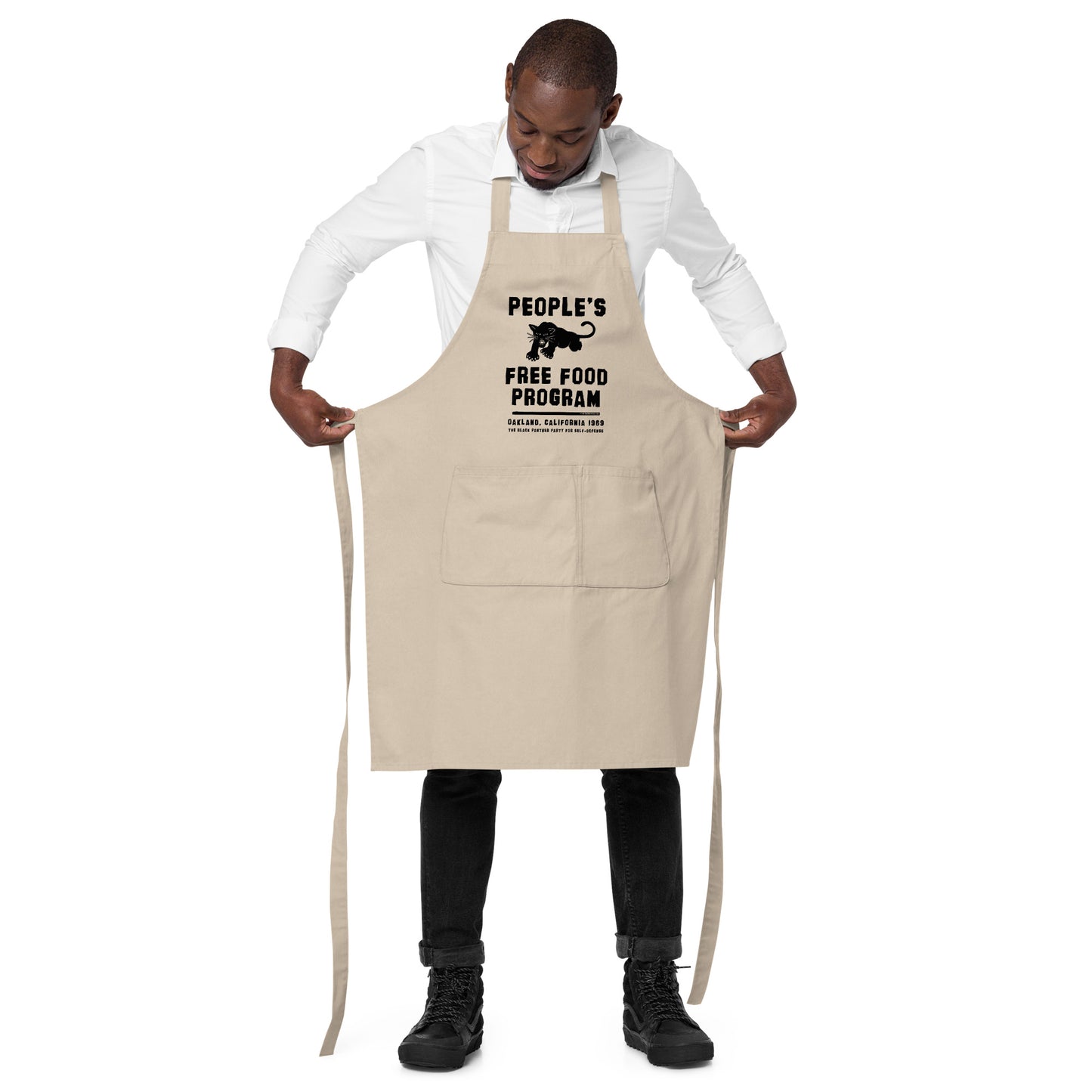 Man adjusting beige BPP People's Free Food Program Organic Cotton Apron with large front pocket and bold civil rights design.
