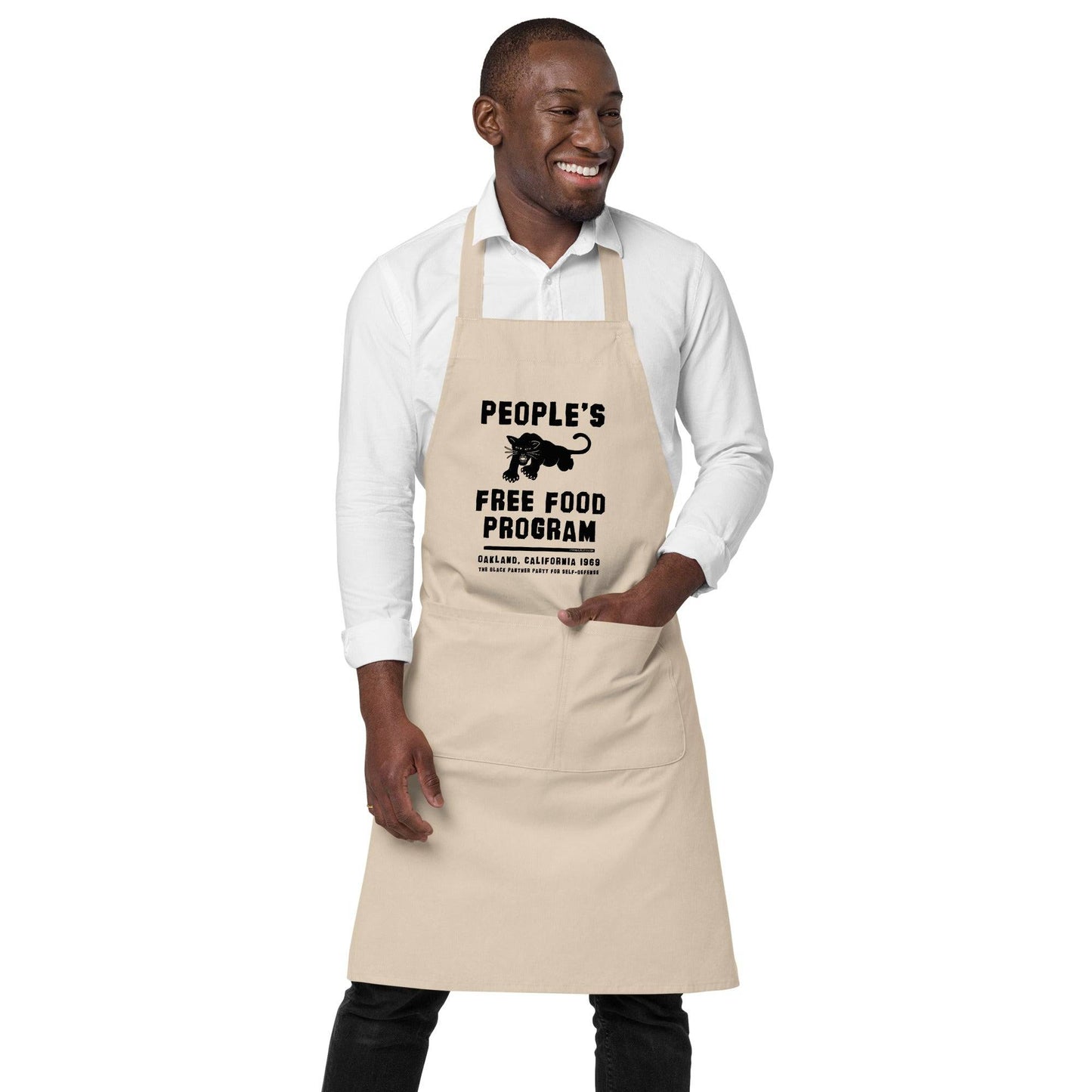 BPP People's Free Food Program Organic Cotton Apron in beige worn by smiling man, featuring bold black panther graphic and historic civil rights text.