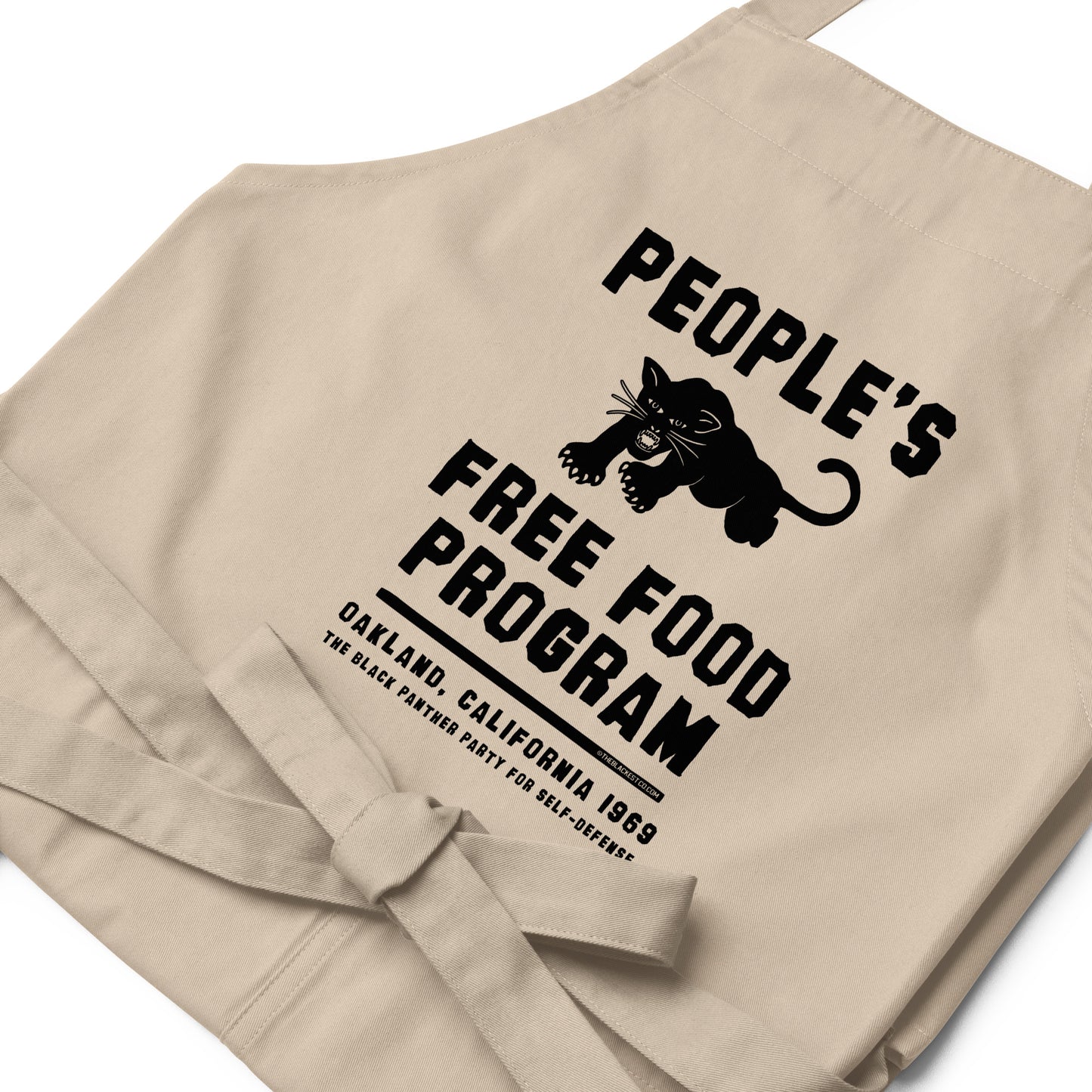 Close-up of beige BPP People's Free Food Program Organic Cotton Apron showing detailed black panther logo and Oakland 1969 civil rights message.