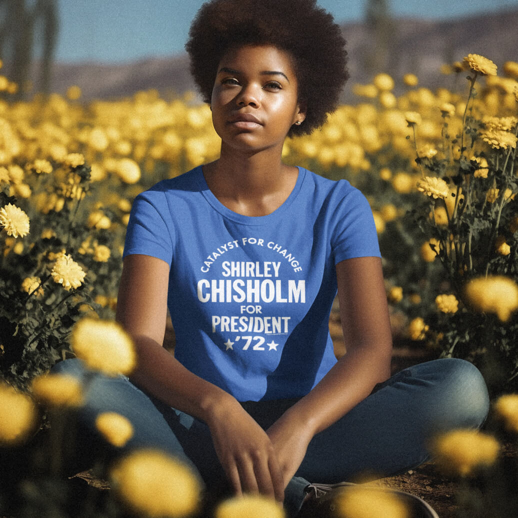 Woman wearing Shirley Chisholm For President 72 Women’s Softstyle T-shirt in blue, seated in a yellow flower field. Feminist graphic tee with vintage style.