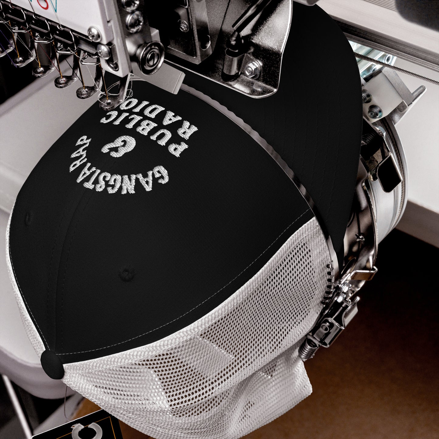 Close-up of embroidery process on Gangsta Rap & Public Radio Retro Trucker Cap, showing precision stitching on black and white hat.
