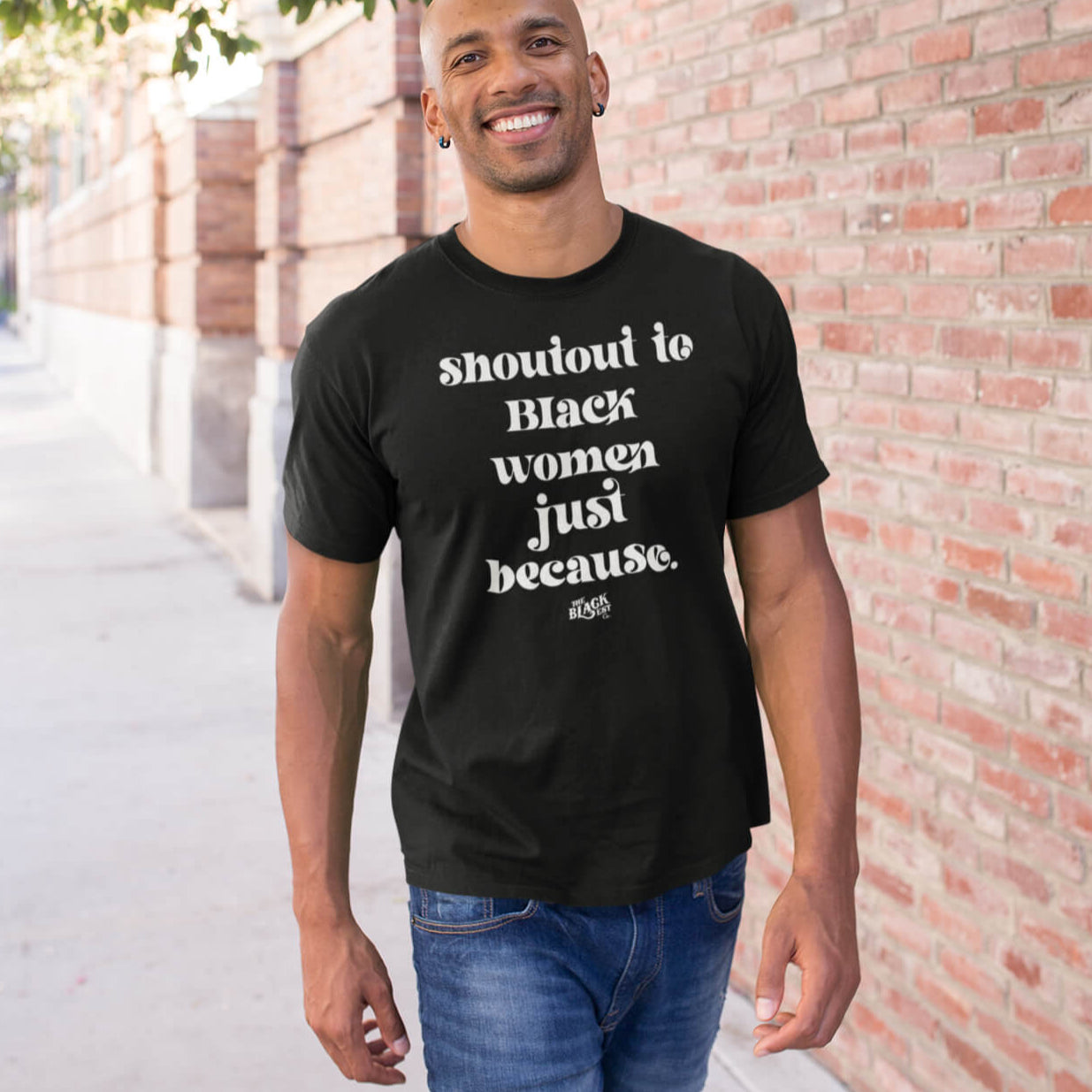 Man wearing the Shoutout To Black Women Just Because Unisex T-Shirt in black, styled casually outdoors. A cultural graphic tee celebrating Black women.