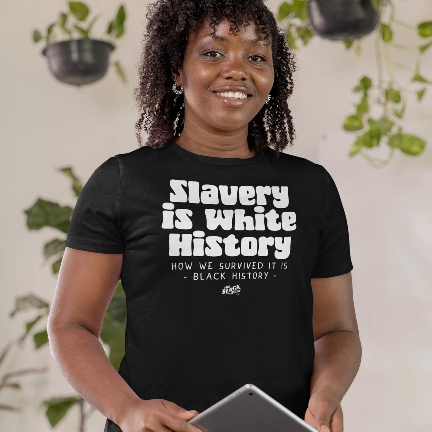Smiling woman wearing a black 'Slavery Is White History' t-shirt. Comfortable and stylish, perfect for Black history awareness and empowerment.