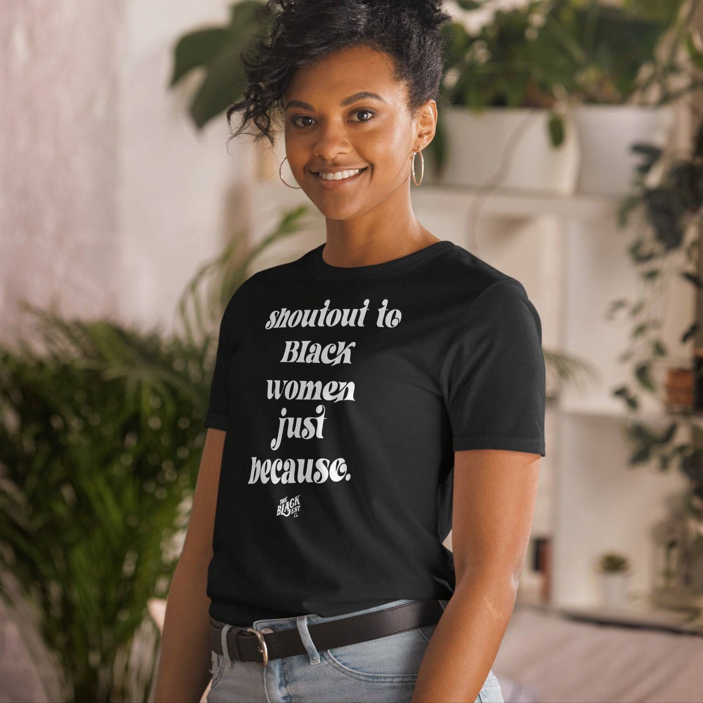 Woman smiling indoors while wearing the Shoutout To Black Women Just Because Unisex T-Shirt. A soft, empowering graphic tee supporting Black culture.