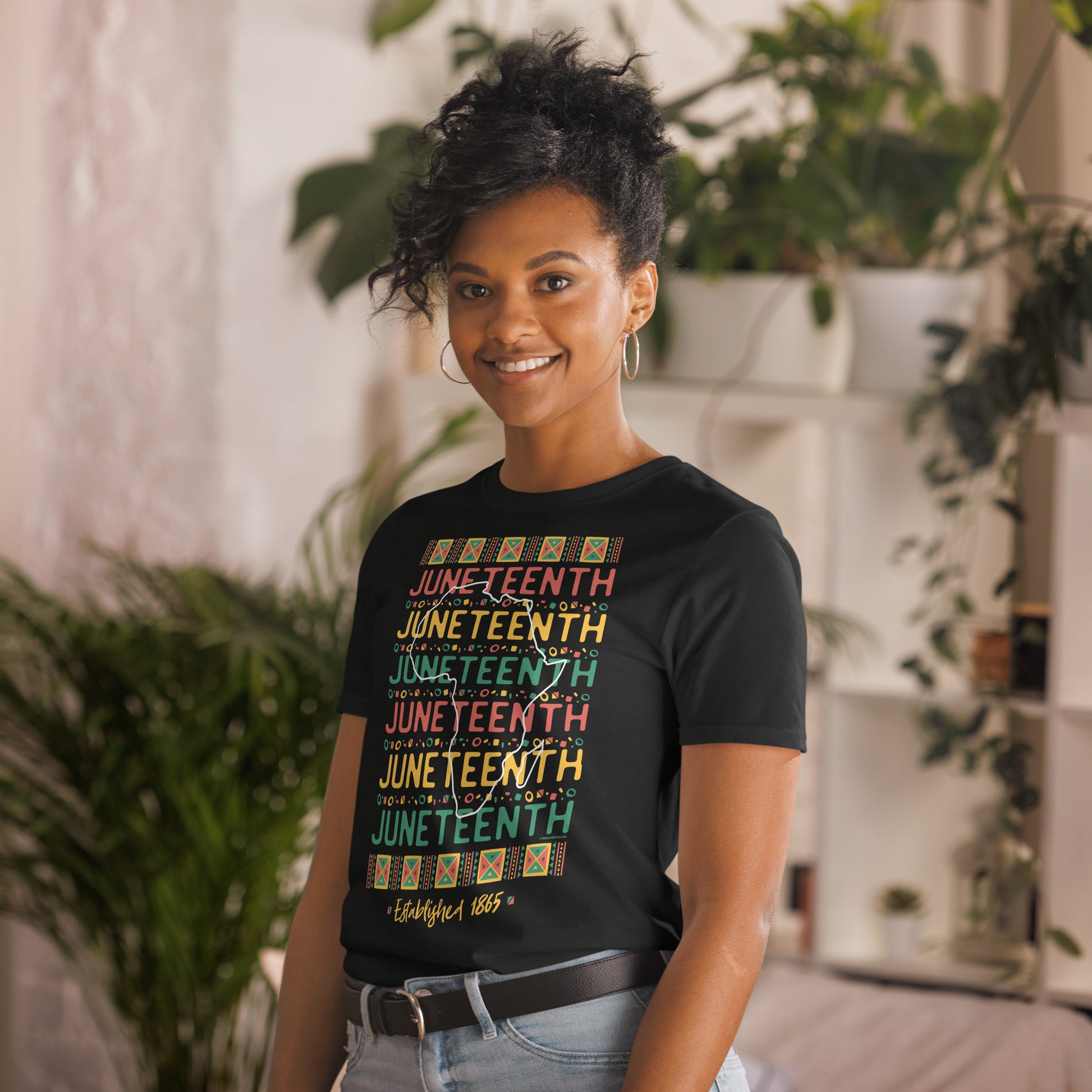 a woman standing in a living room with a plant in the background in t - shirt with the words Juneteenth Repeat Established 1865 on it