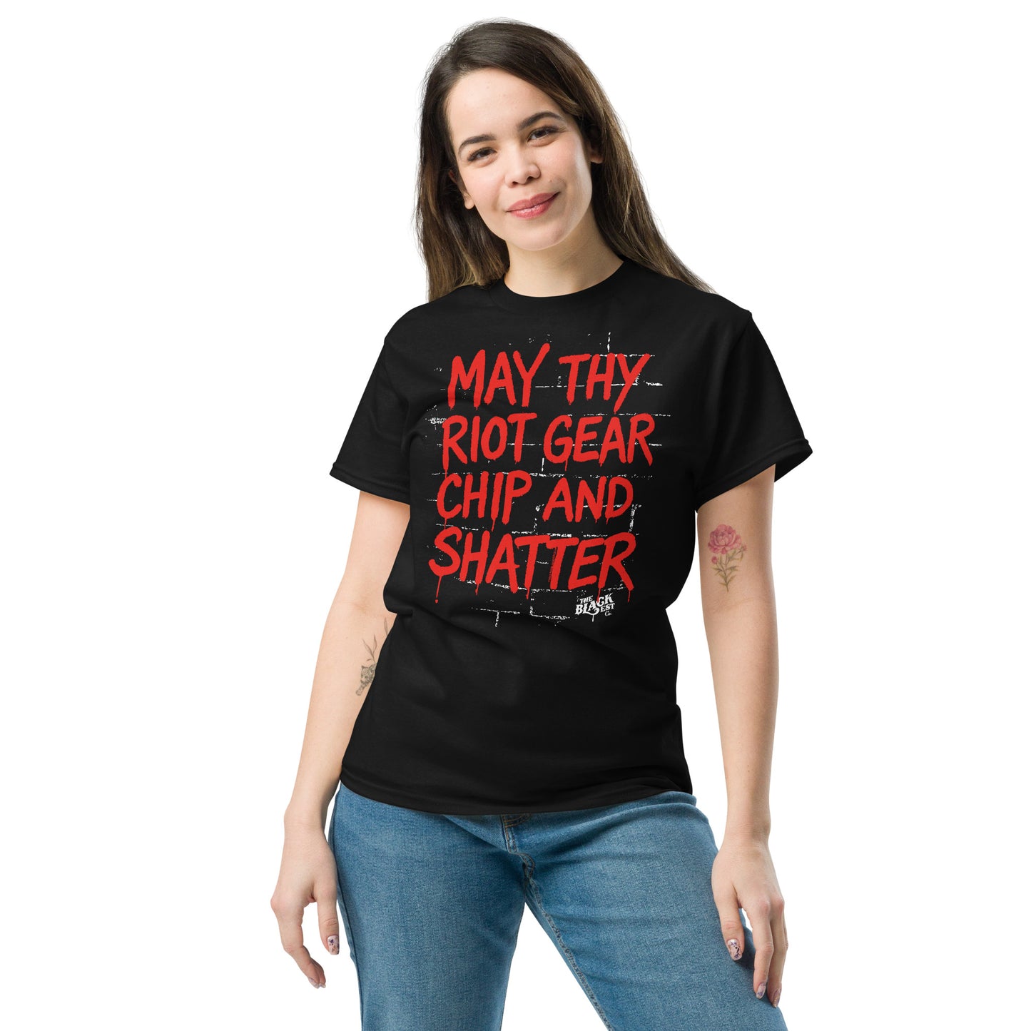 Female model wearing black May Thy Riot Gear Chip And Shatter Staple T-Shirt by TheBlackest Co., styled with jeans for casual protest fashion.