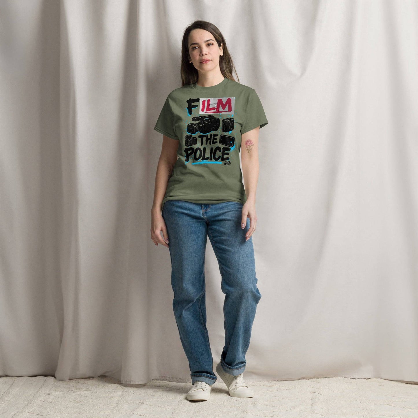 Woman wearing olive green Film The Police Staple T-shirt by TheBlackest Co., styled with jeans in a minimalist indoor setting.
