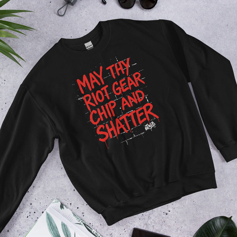 Flat lay of black May Thy Riot Gear Chip And Shatter Unisex Sweatshirt with red protest message, styled with accessories for gifting.