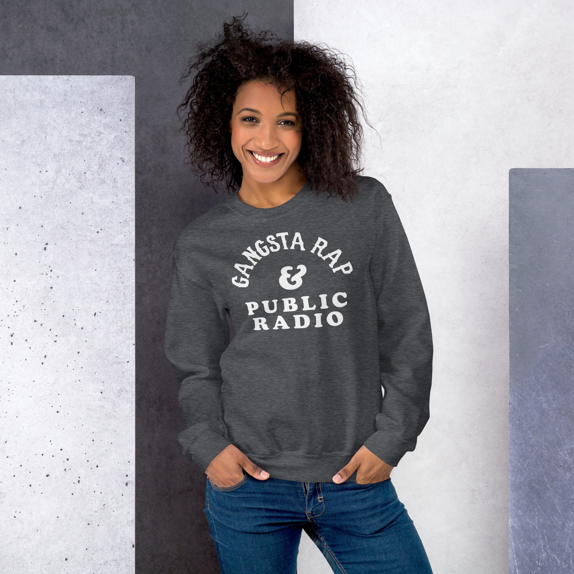 Woman wearing Gangsta Rap And Public Radio Unisex Staple Sweatshirt in dark heather gray, showcasing cozy fit and cultural statement design.