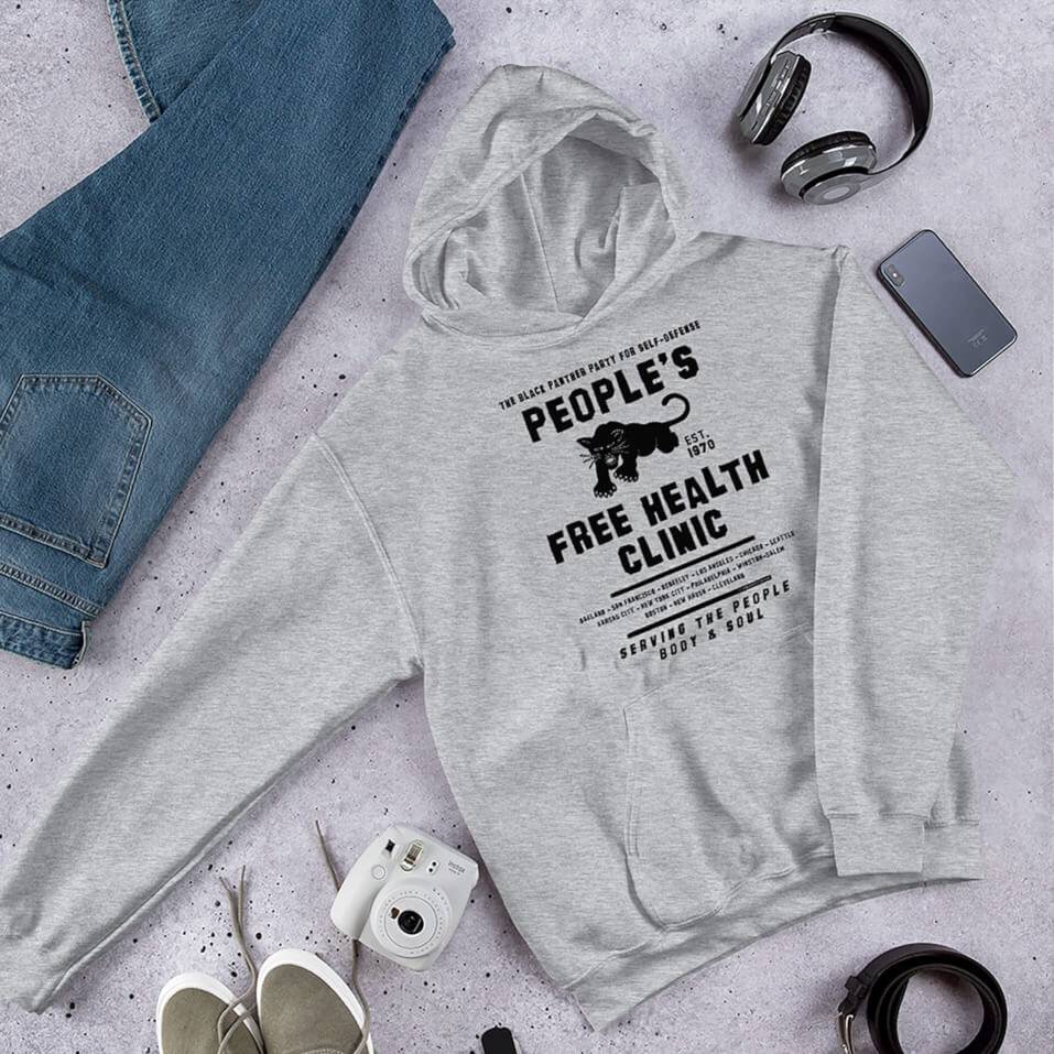 Gray People's Free Health Clinic BPP Unisex Pullover Hoodie with bold black text and graphic, styled flat with jeans, headphones, and accessories.