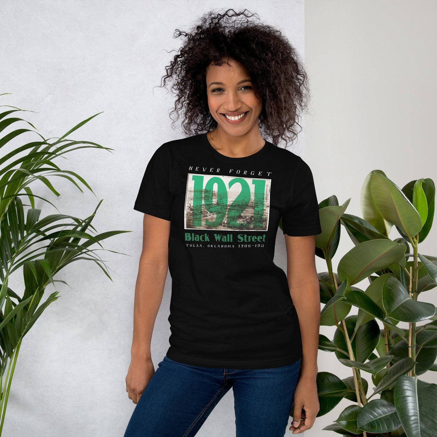 Woman in Black Wall Street 1921 t-shirt, standing by plants.