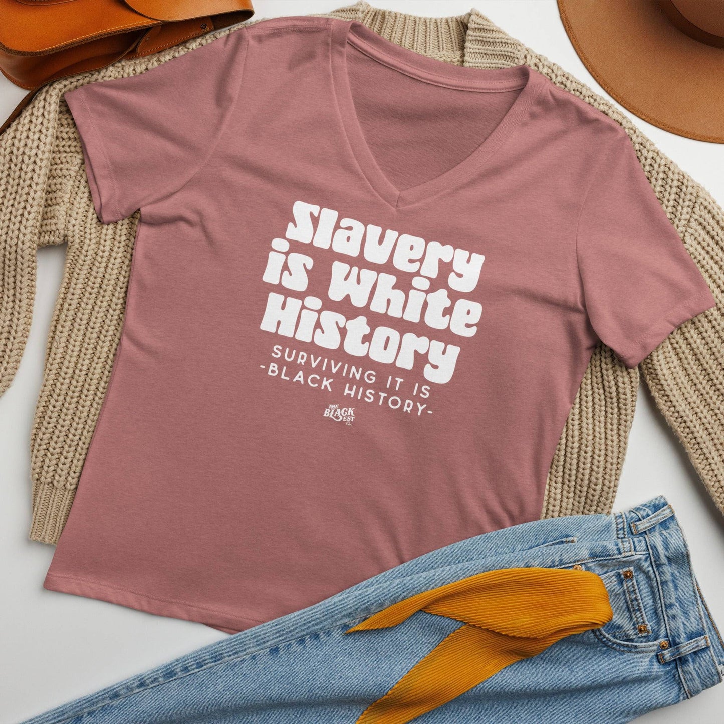 Flat lay of the ALLY Slavery Is White History Women's V-neck T-shirt in mauve, paired with jeans and accessories for a stylish, message-driven outfit.