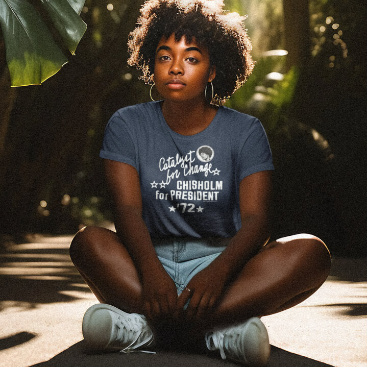 Woman wearing navy Shirley Chisholm Vintage Campaign Women’s Softstyle T-shirt, seated outdoors, showcasing soft fit and empowering message.
