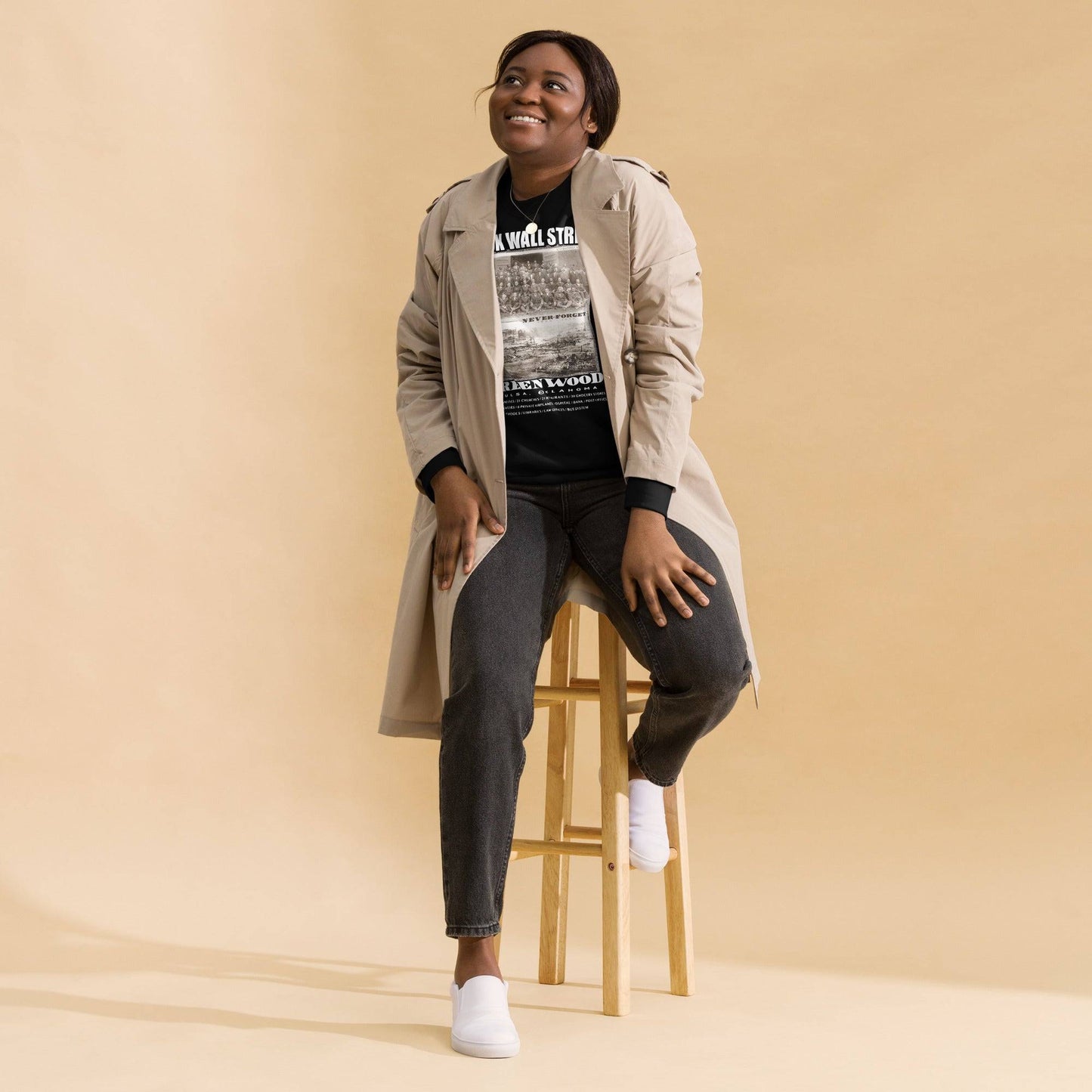 woman sitting on a chair wearing a black premium sweatshirt with writing that says Black Wall Street and Greenwood