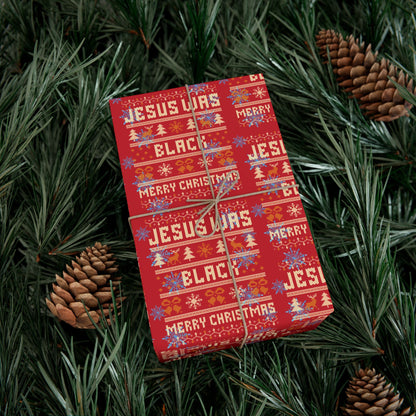 Christmas gift wrapped in Jesus Was Black Merry Christmas red paper surrounded by pinecones and greenery, bold and festive wrap.