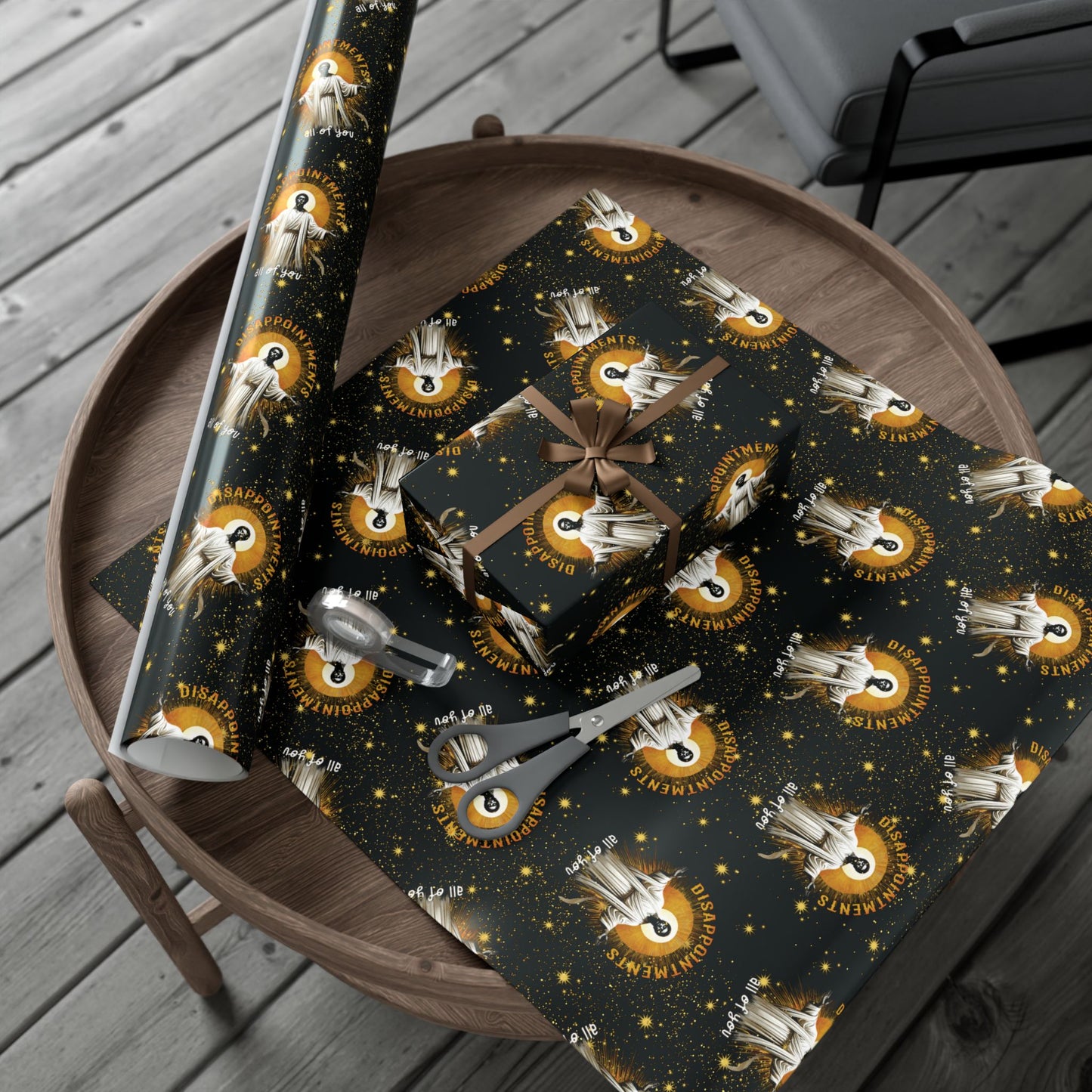 Black Jesus Disappointments All Of You Christmas Gift Wrap on a table with scissors and ribbon, showcasing its matte finish and playful holiday theme.