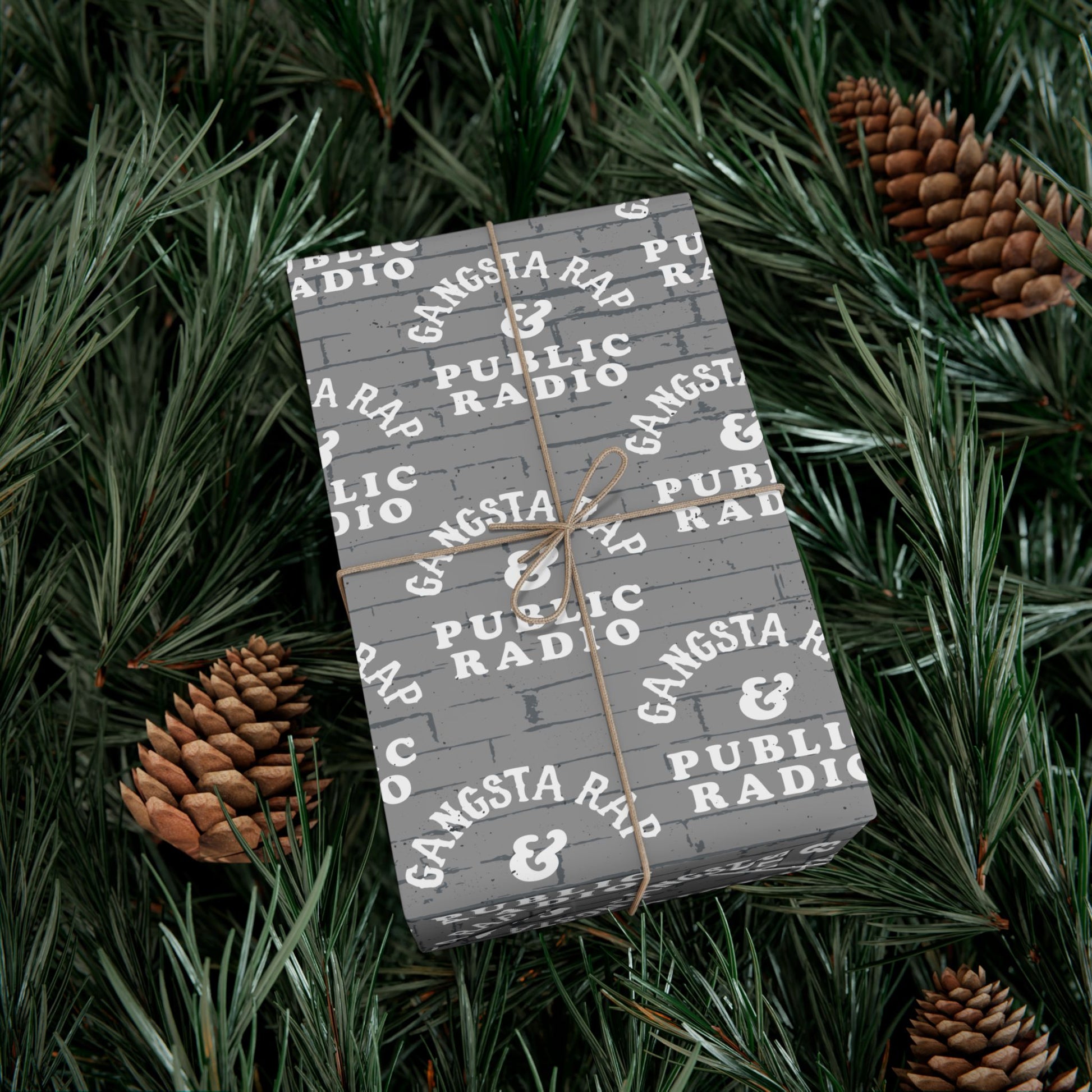 Gangsta Wrap & Public Radio Christmas Wrapping Paper on a gift nestled in pine branches, festive and urban-themed for holiday decor.