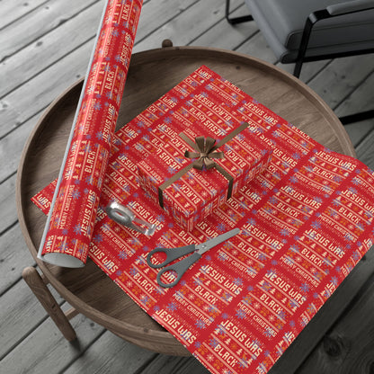 Red Jesus Was Black Merry Christmas wrapping paper roll and wrapped gifts on wooden table, perfect for statement holiday gift wrap.