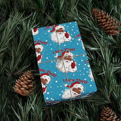 Holiday gift wrapped in Black Santa 'I Saw That!' Christmas paper, surrounded by pinecones for a festive seasonal display.