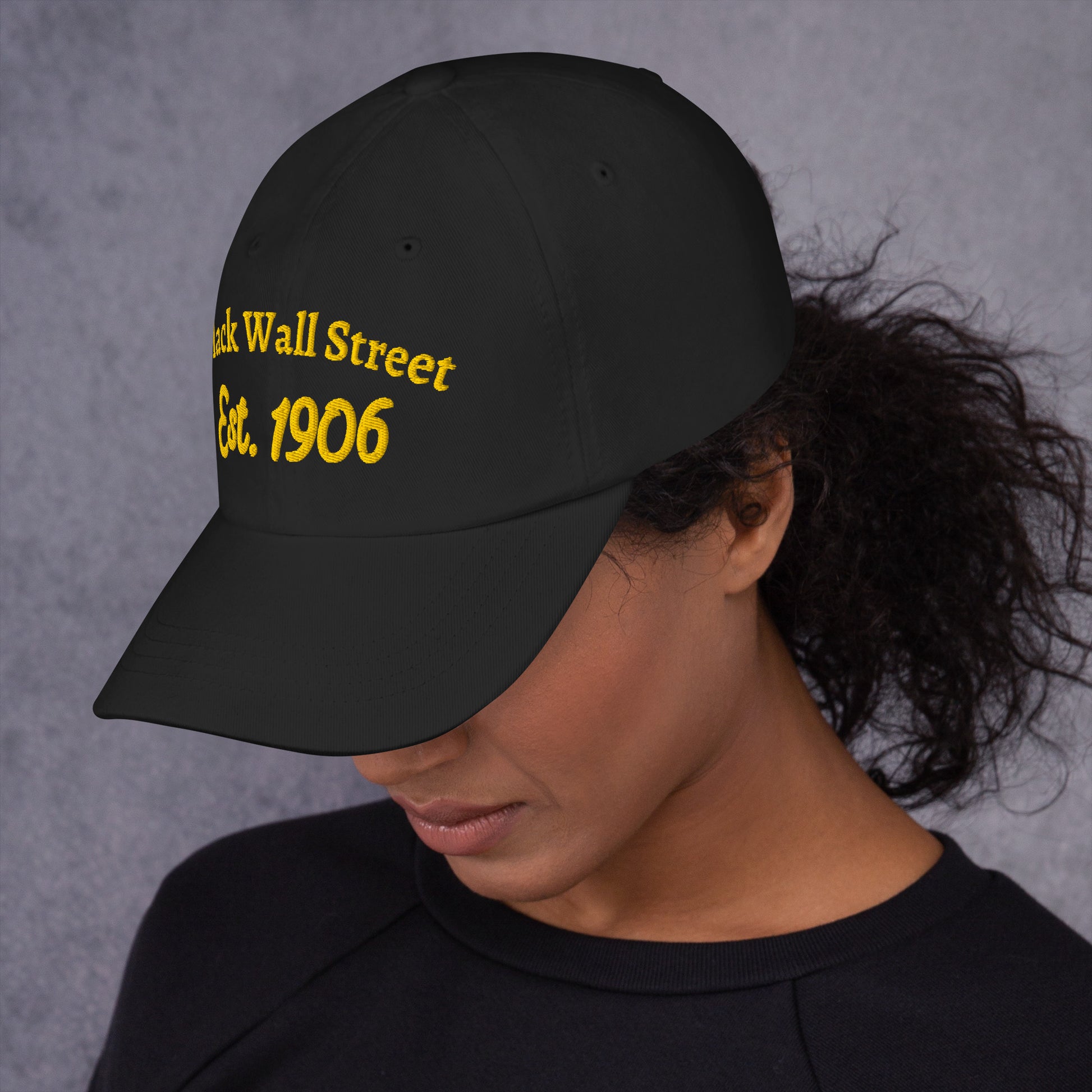 Woman wearing Black Wall Street Est. 1906 Baseball Cap, showcasing curved visor and embroidered front in yellow thread.