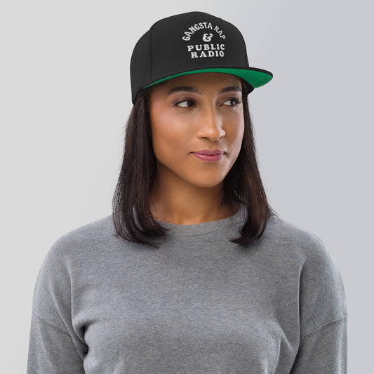 a woman wearing a black and green hat with gansta rap & public radio embroidery on it