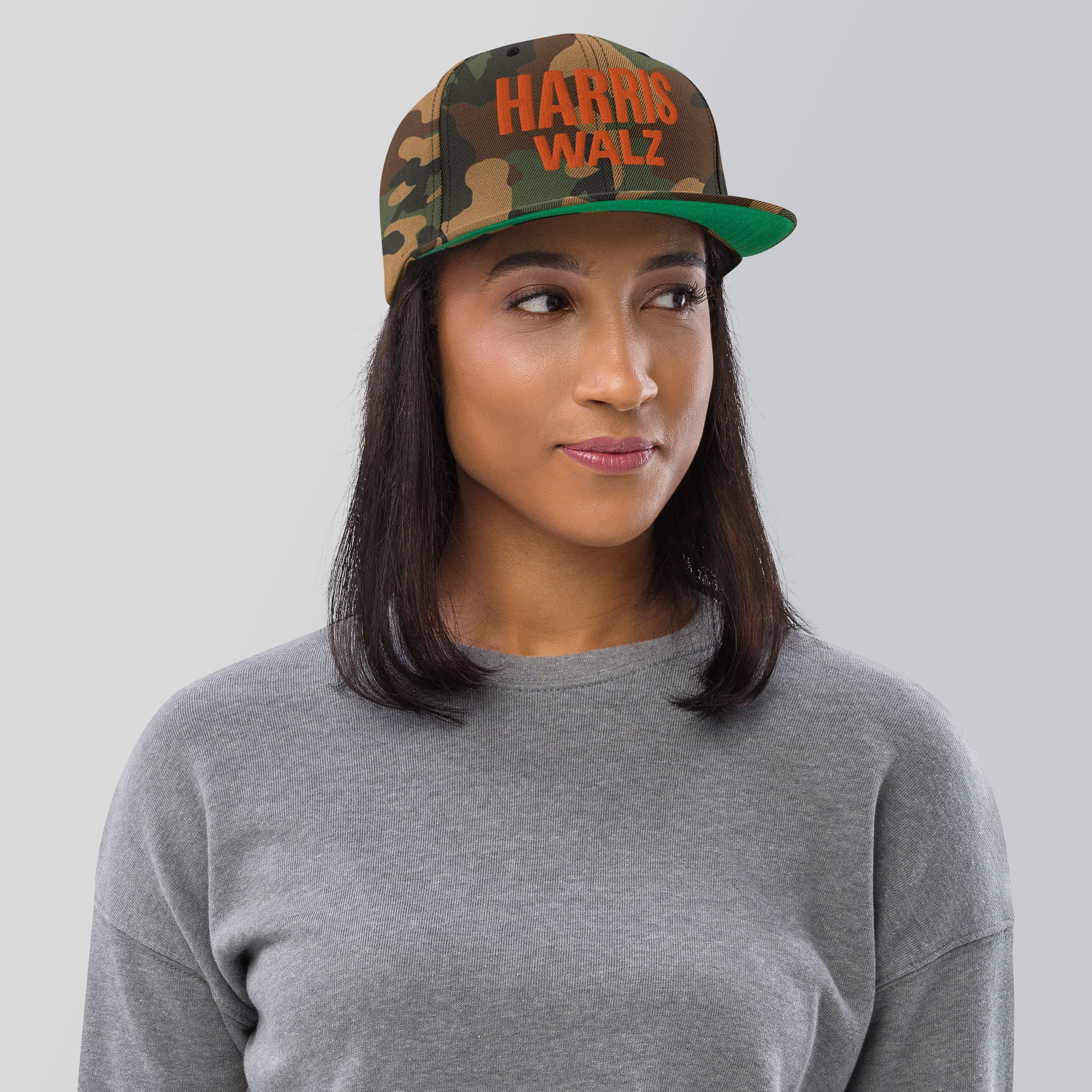 Classic snapback cap in green camo with front Harris Walz orange embroidery, adjustable fit.