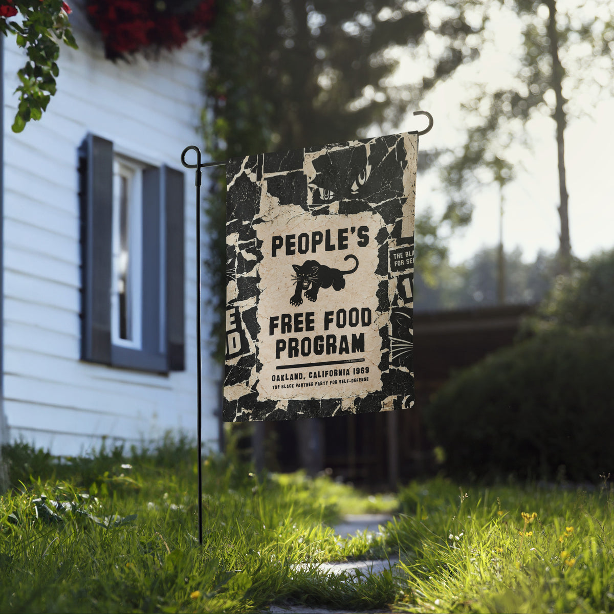 Black Panther Party People's Free Food Program garden flag on a black stand in a front yard beside a white house