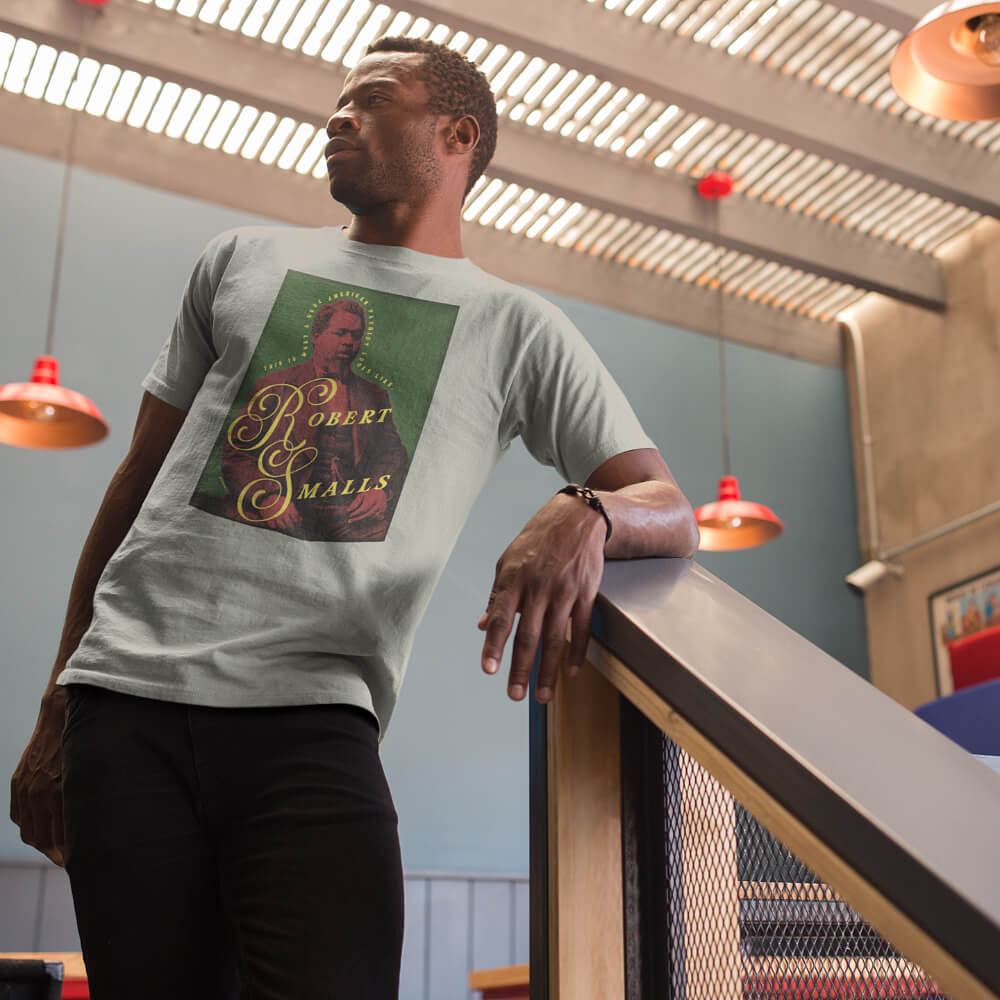 Man wearing a Robert Smalls American Hero Heavyweight Premium T Shirt featuring a bold vintage-style graphic of Robert Smalls in red, green, and yellow tones. Ideal for fans of historical figures and Black heritage apparel.