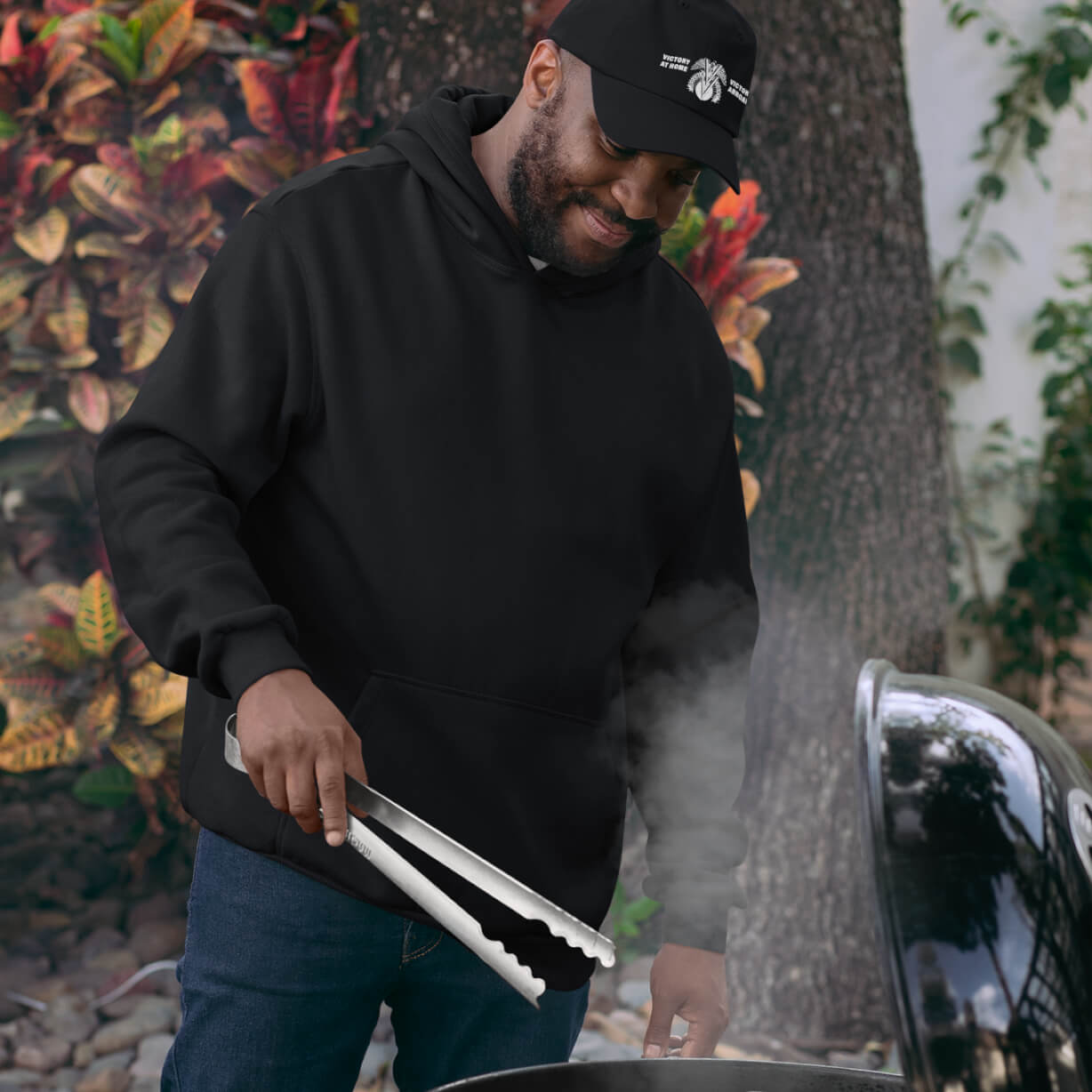 Man wearing the Double V Campaign Victory Home Abroad Baseball Cap while grilling outdoors, showcasing casual fit and cultural pride.