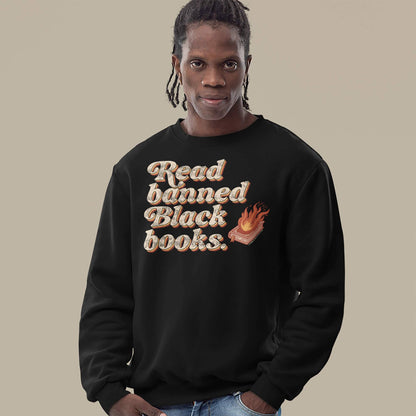 Man wearing a black 'Read Banned Black Books' sweatshirt, featuring bold text and a flaming book graphic, ideal for cultural expression and cold weather.