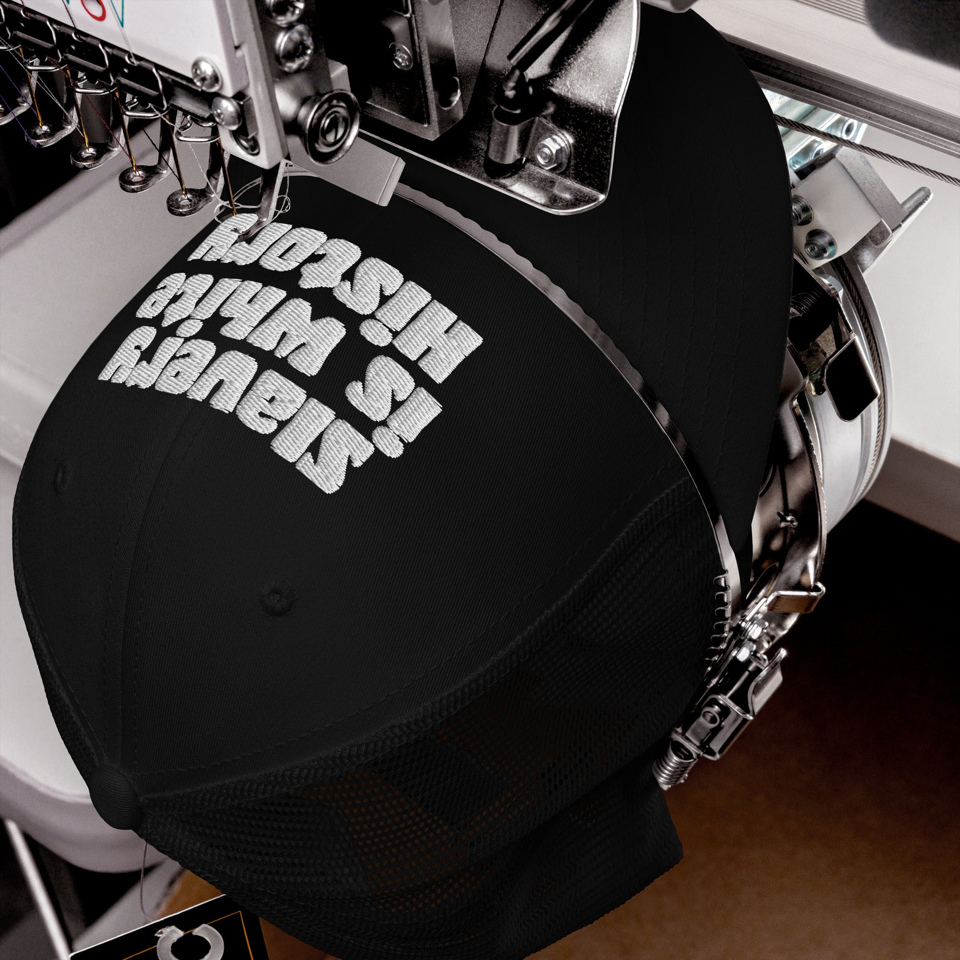 Close-up of embroidery machine stitching Slavery Is White History on black trucker hat by TheBlackest Co., made in the USA.