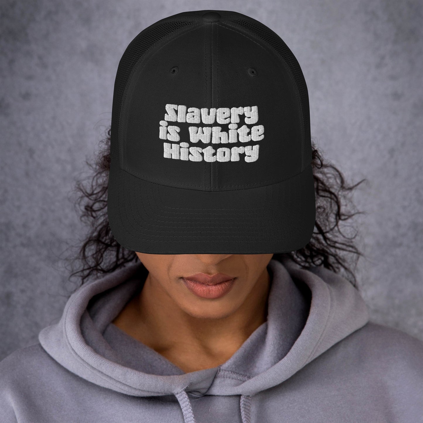 Woman wearing Slavery Is White History Trucker Hat by TheBlackest Co., showcasing bold embroidered message and structured front panel.
