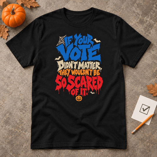 Black t-shirt reading "If Your Vote Didn't Matter, They Wouldn't Be So Scared Of It" in blue, cream and dripping red Halloween lettering with bats and a jack-o'-lantern, laid flat beside a pumpkin and a ballot