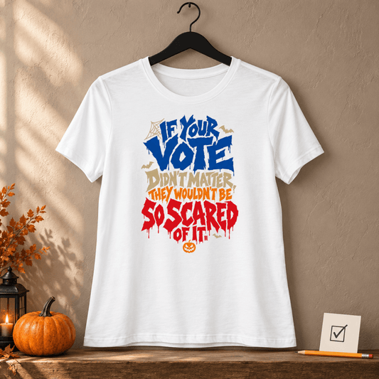 White women's relaxed t-shirt reading "If Your Vote Didn't Matter, They Wouldn't Be So Scared Of It" in blue, cream and dripping red Halloween lettering with bats and a jack-o'-lantern, on a hanger beside a pumpkin