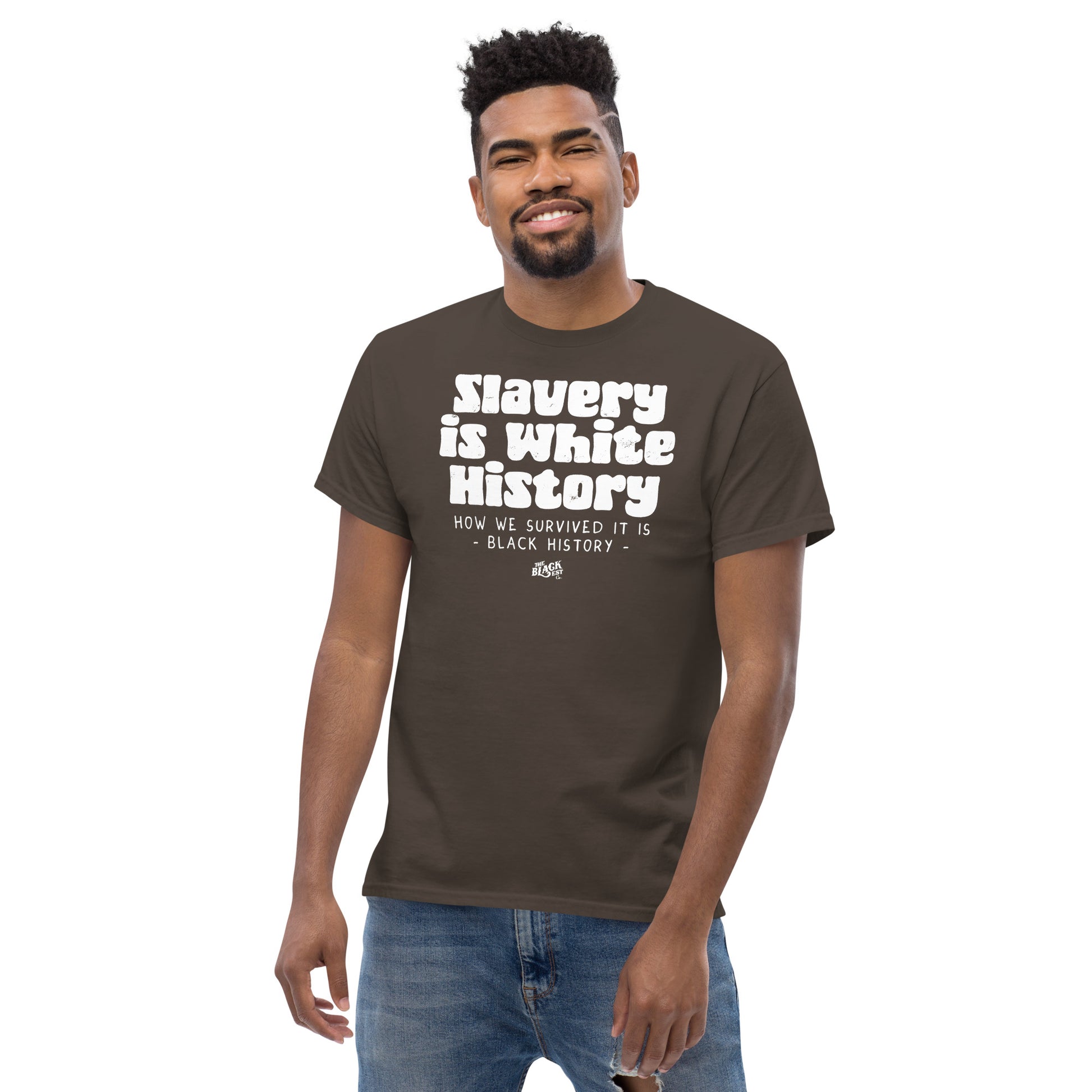 Man wearing a brown unisex t-shirt with the phrase 'Slavery Is White History, How We Survived It Is Black History,' standing confidently.