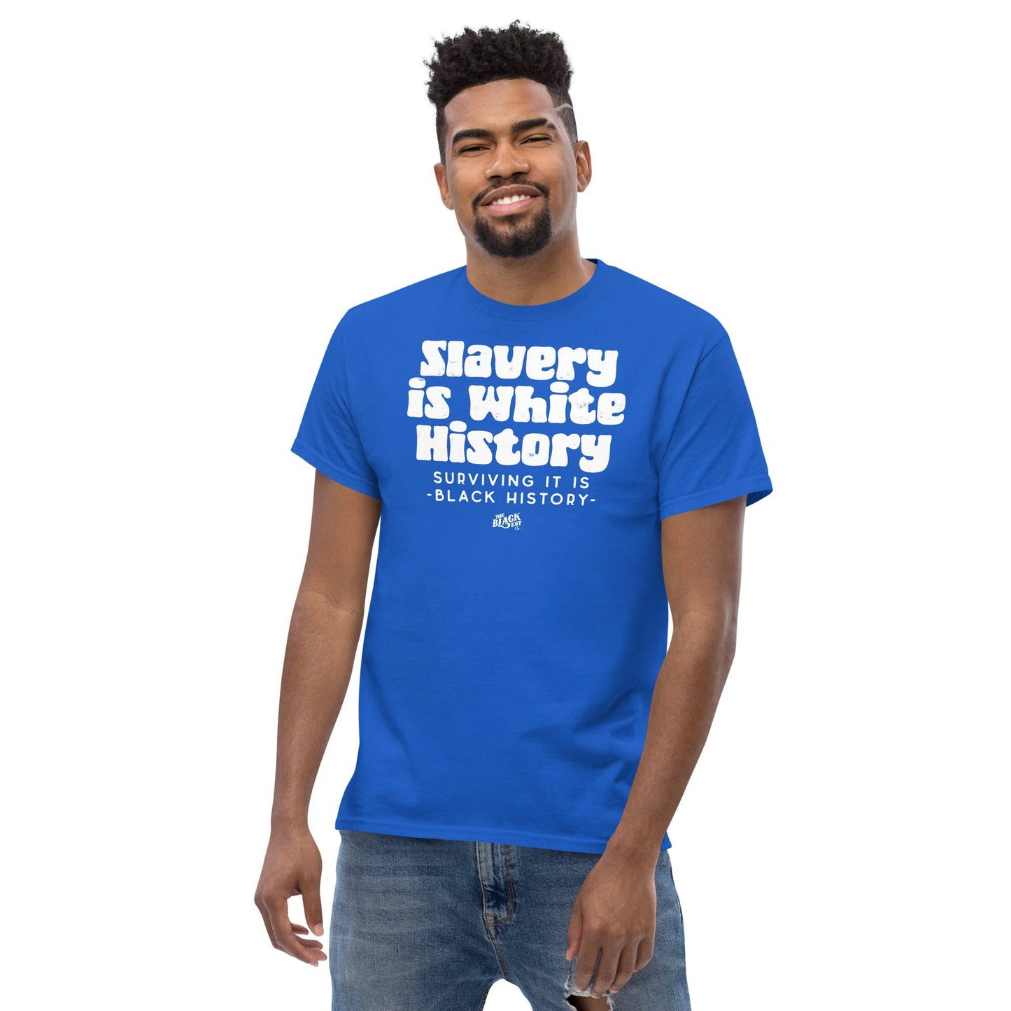 Man smiling while wearing a blue t-shirt with the text 'Slavery Is White History, Surviving It Is Black History' by TheBlackest Co.