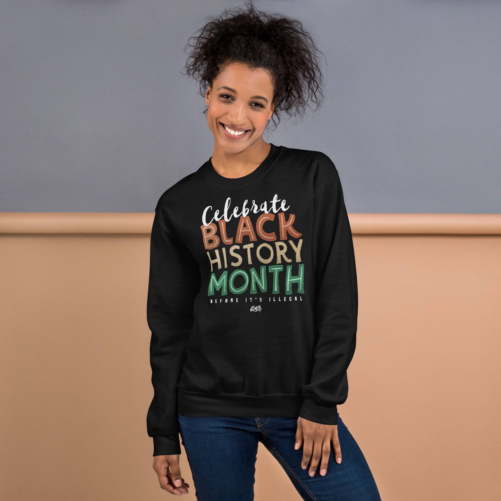 Smiling woman wearing a black 'Celebrate Black History Month Before It’s Illegal' sweatshirt. Stylish and comfortable for casual wear.