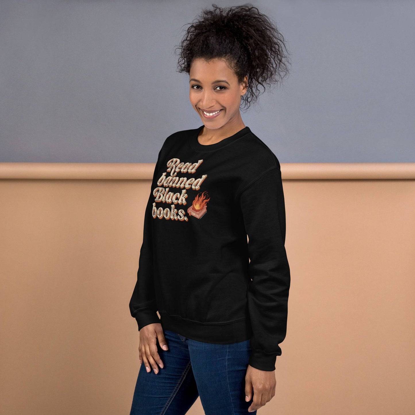 Woman smiling in a black 'Read Banned Black Books' sweatshirt, showcasing bold lettering and a flaming book design, perfect for casual wear and cultural pride.