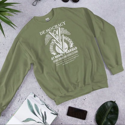 Flat lay of olive green Double V Campaign WWII Black Soldiers Sweatshirt with historical print, styled with plants and a book for lifestyle appeal.