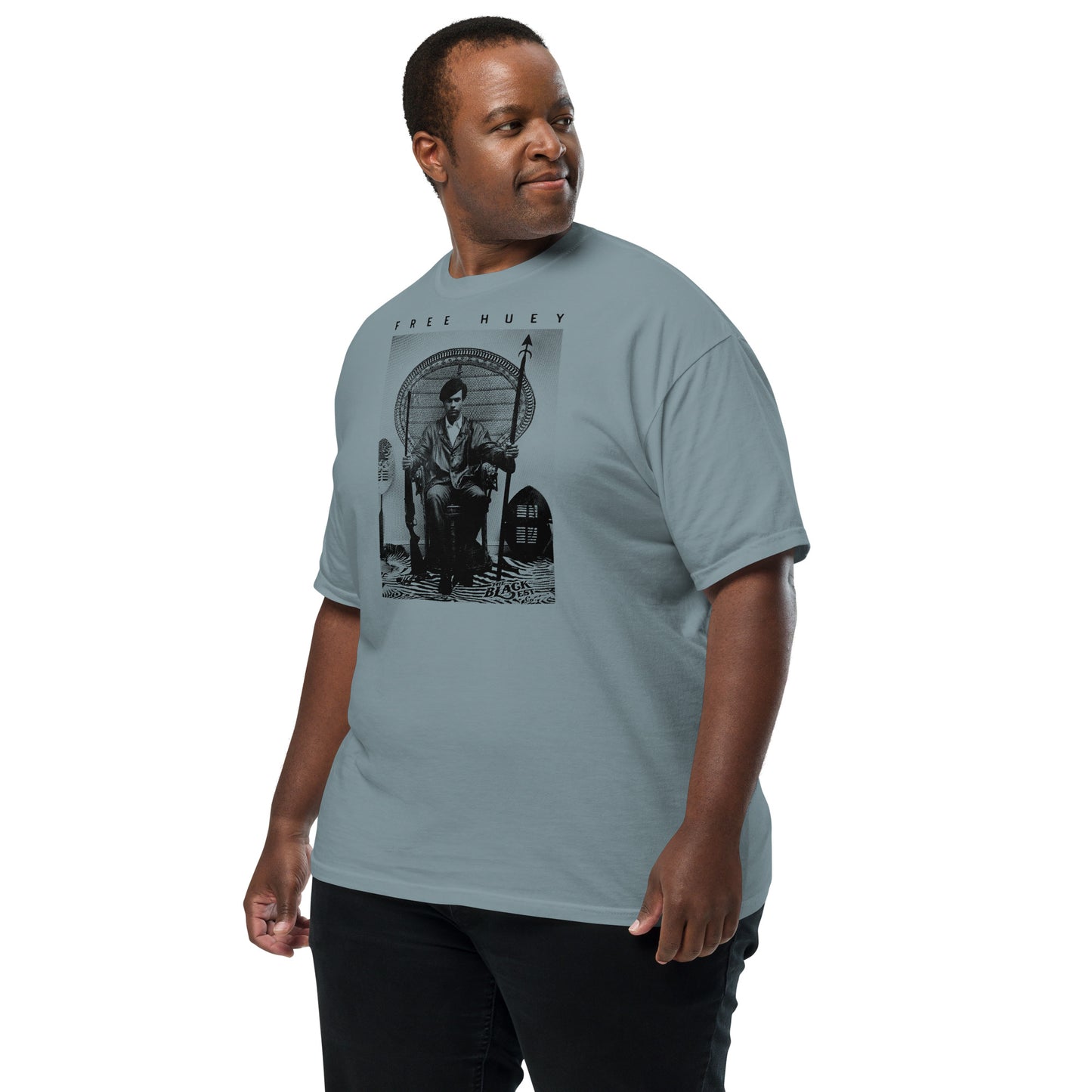 man wearing a blue t shirt with a picture of huey p newton sitting on a wicker chair