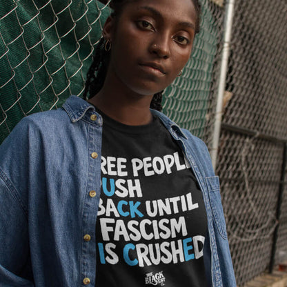 Model wearing black protest T-shirt with slogan in front of chain-link fence